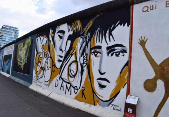 Black and gold East Side Gallery mural featuring faces and the word 'D'AMOR'