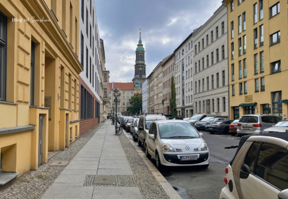 Street view in Berlin Mitte with parked cars, classic residential buildings and the tower of St. Nicholas Church in the distance