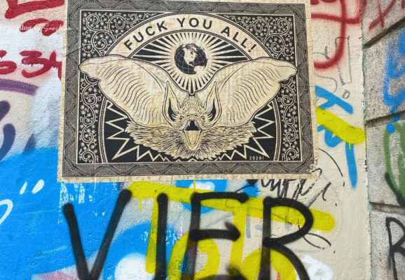Street art poster of a bat with bold message and world graphic surrounded by colorful Berlin graffiti wall