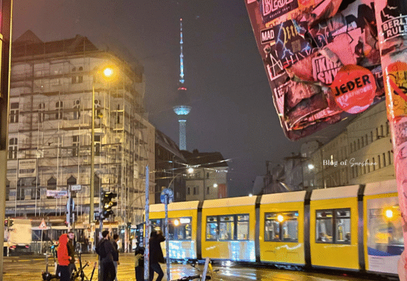 Night view of Berlin's iconic TV Tower with a yellow tram passing by in the rain near Alexanderplatz