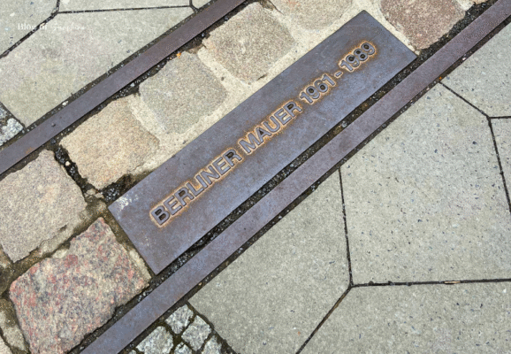 Close-up of the Berlin Wall ground marker with the inscription ‘Berliner Mauer 1961–1989’ embedded between cobblestones in Berlin