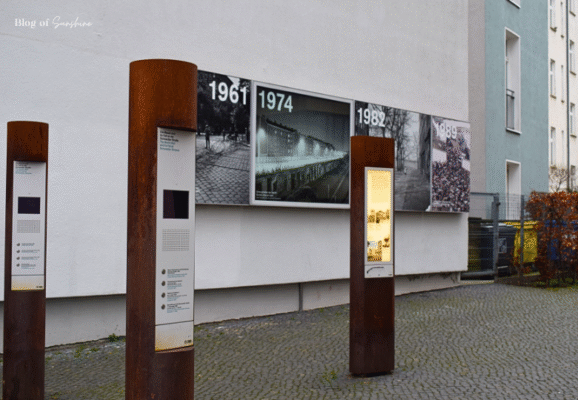 Berlin Wall Memorial at Bernauer Straße showing rusted steel information pillars and historic photo timeline from 1961 to 1989 on a residential building wall