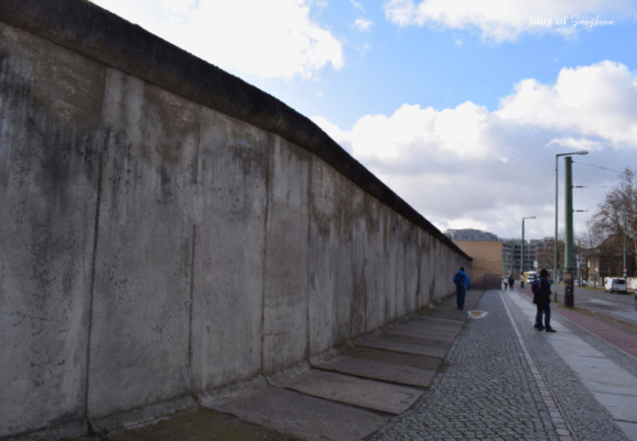 Long preserved stretch of the original Berlin Wall along the street, with visitors walking alongside the historic concrete barrier