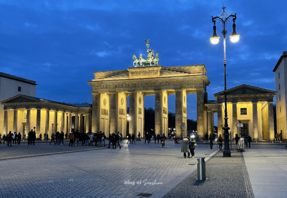 Brandenburg Gate illuminated at night in Berlin, glowing with golden lights against the evening sky