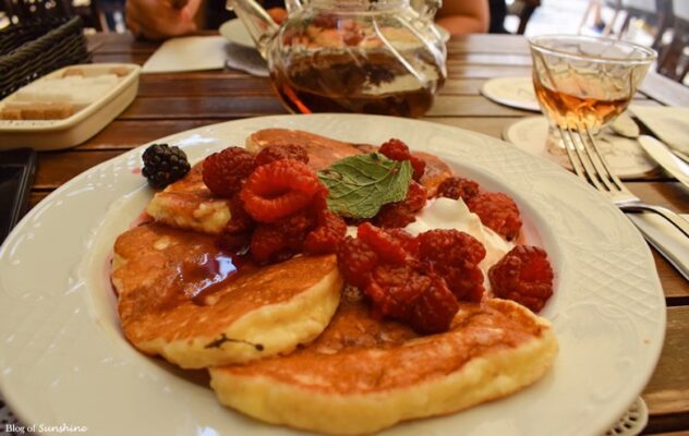Fluffy pancakes topped with raspberries, whipped cream, and mint served with tea at Centaur café on Rynok Square in Lviv