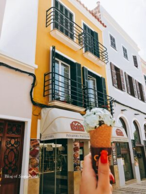 Holding ice cream in front of a pastel-colored building and bakery café in Ciutadella’s old town, Menorca