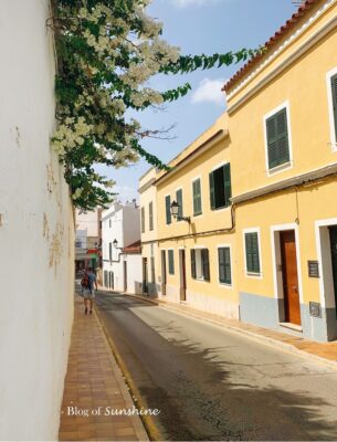 Quiet yellow street in Ciutadella, Menorca with white bougainvillea flowers and traditional shutters