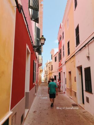 People walking down a colorful narrow street in the old town of Ciutadella, Menorca surrounded by historic buildings