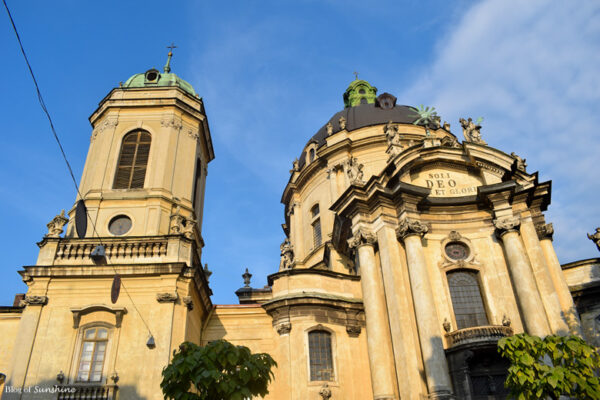 Close-up of the Dominican Church in Lviv with its green dome, twin towers, and ornate Baroque façade under a blue sky