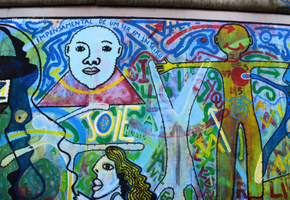 Colorful surreal mural with human figures and text on the East Side Gallery in Berlin