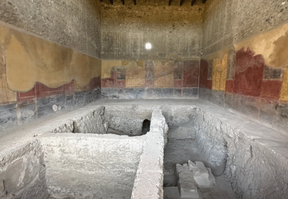 Interior of a frescoed room in the House of the Vettii, Pompeii, showing ongoing excavation of buried structures.
