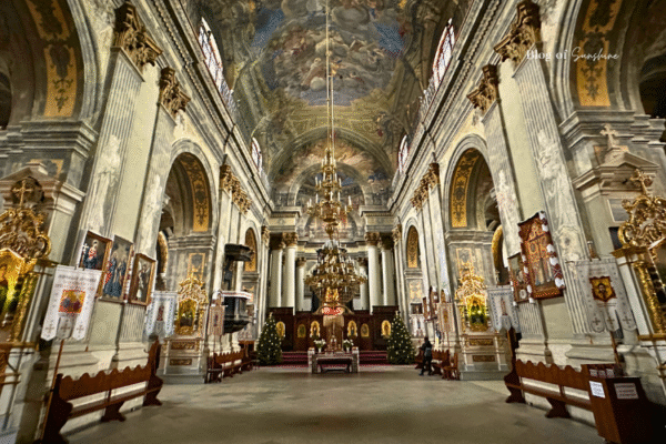 Interior of the Jesuit Church in Lviv, Ukraine, with grand baroque design, ornate chandeliers, golden icons, and vivid ceiling frescoes.