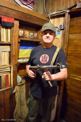 Man dressed in military-style clothing holding a prop gun at the entrance of Kryivka, the secret bar in Lviv, Ukraine