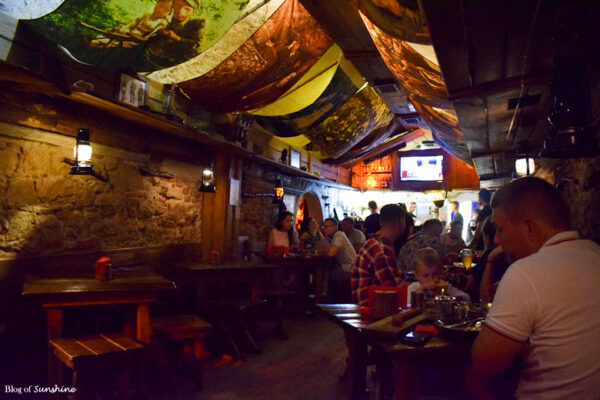 Interior of Kryivka underground bar in Lviv, with diners seated under colorful ceiling banners in a dim, bunker-like setting