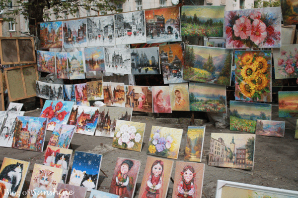 Vibrant handmade paintings of Lviv architecture, flowers, and characters displayed at an outdoor market