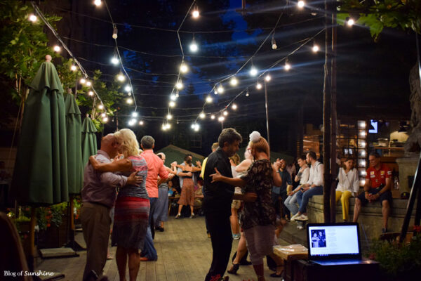 Couples dancing under string lights at an outdoor café bar near the Fountain of Diana in Lviv at night