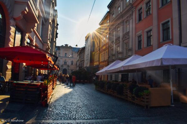 Sunset casting golden light over a cobbled street lined with outdoor cafés and colorful umbrellas in Lviv Old Town, Ukraine