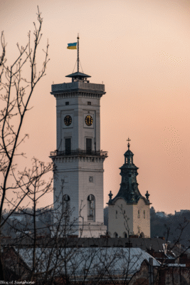 Lviv Town Hall clock tower at sunset with Ukrainian flag flying and church dome in the background
