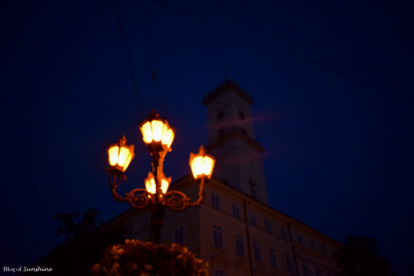 Warmly lit street lamps in front of Lviv Town Hall at night in the city’s historic center