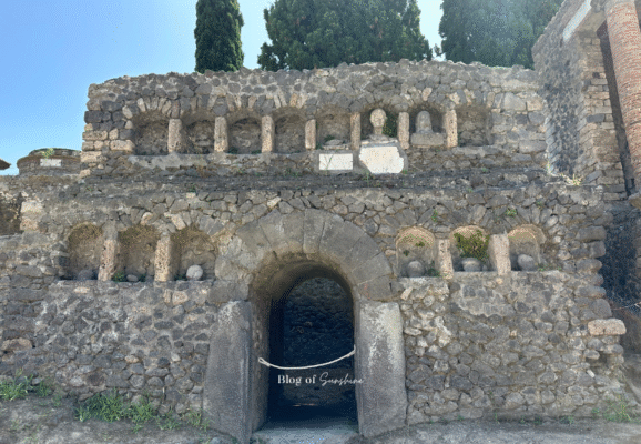 Ancient Roman columbarium in Pompeii near Porta Nocera, featuring stone niches with memorial busts and an arched tomb entrance