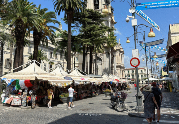 Colorful street market in modern Pompeii near the Basilica, with stalls selling souvenirs, local crafts, and Italian flags under palm trees