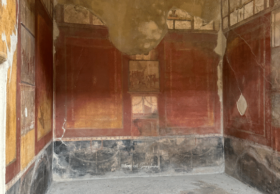 Room in the House of the Vettii, Pompeii, featuring red and black Fourth Style frescoes with mythological scenes.