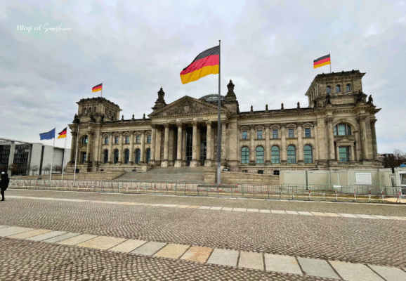 The Reichstag building in Berlin with German flags flying, featuring its historic façade and modern glass dome