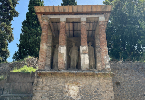Roman funerary monument along Pompeii’s Via delle Tombe featuring life-sized statues behind brick columns