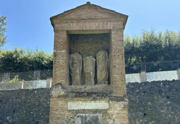 Brick funerary monument in Pompeii with three draped Roman statues inside a niche, dedicated to Vesonius
