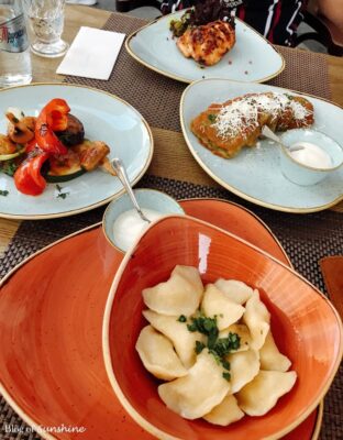 A table full of traditional Ukrainian dishes at Otset restaurant in Lviv, featuring vareniki dumplings, grilled vegetables, potato pancakes, and chicken filet