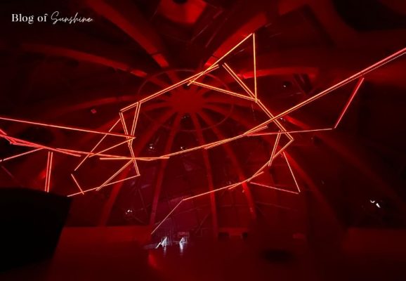 Angular red light sculpture hanging from the ceiling of an Atomium exhibition sphere