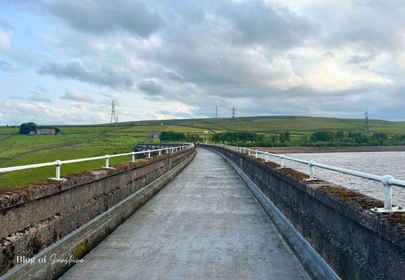 Concrete path with railings along the top of Baitings Reservoir dam halfway through the circular walk