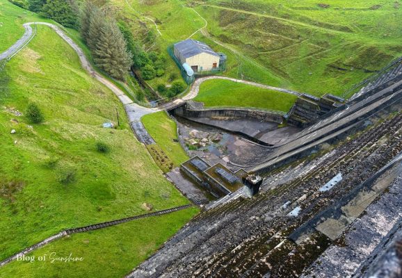 Looking down from the top of Baitings Reservoir dam to the spillway, control building and steep grassy valley below