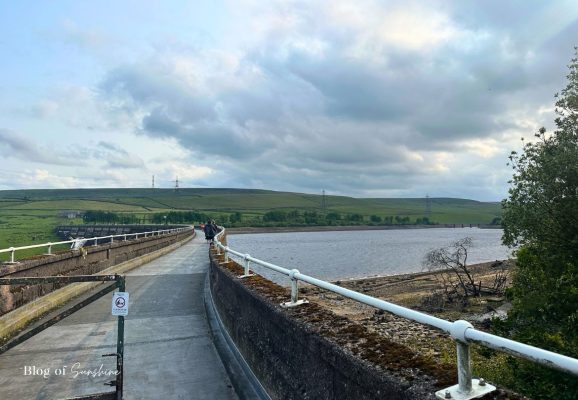 People walking along the top of Baitings Reservoir dam at the start of the circular walk near Rishworth