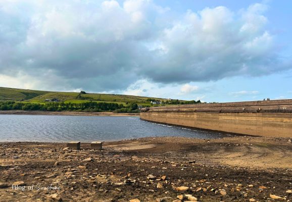 Shoreline view of Baitings Reservoir with the dam wall curving away and green hills in the background