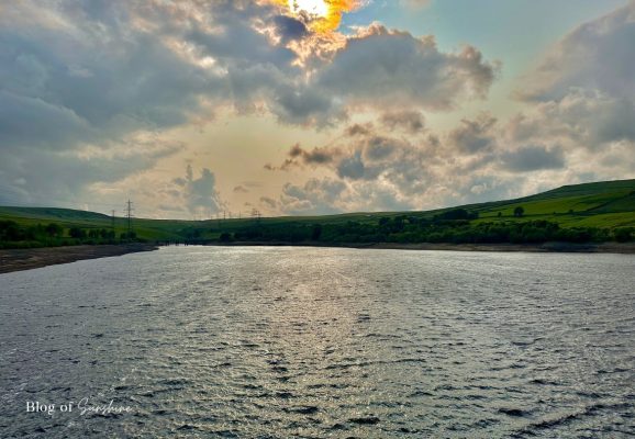 Wide view across Baitings Reservoir from the dam wall with rippling water, moorland hills and dramatic evening clouds