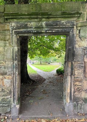 Old stone doorway framing a path and trees in the grounds of Hexham Abbey