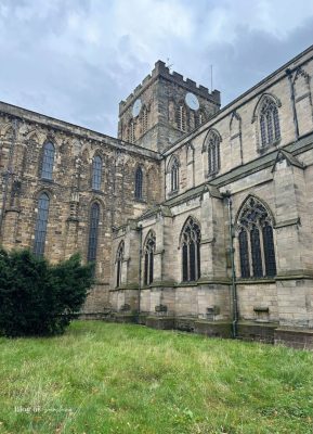 Hexham Abbey tower with clock faces and Gothic arched windows above a grassy churchyard