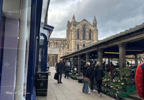 People browsing market stalls in Hexham Market Place with Hexham Abbey in the background