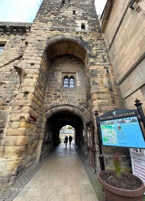 People walking through the archway of Hexham’s Moot Hall beside a Welcome to Hexham sign