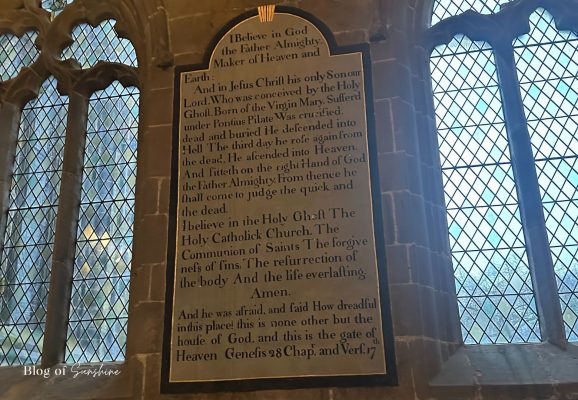 Historic painted text board beside leaded windows in St John the Baptist Church Tideswell