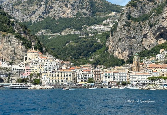 View of Amalfi town from the water with harbour, pastel buildings and mountains on the Amalfi Coast