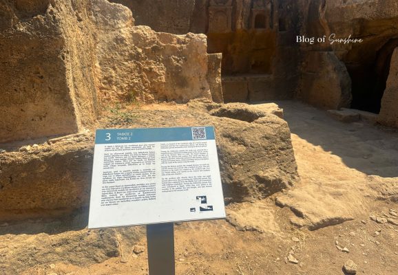 Information sign for Tomb 2 at Tombs of the Kings in Paphos Cyprus with rock-cut chambers behind it