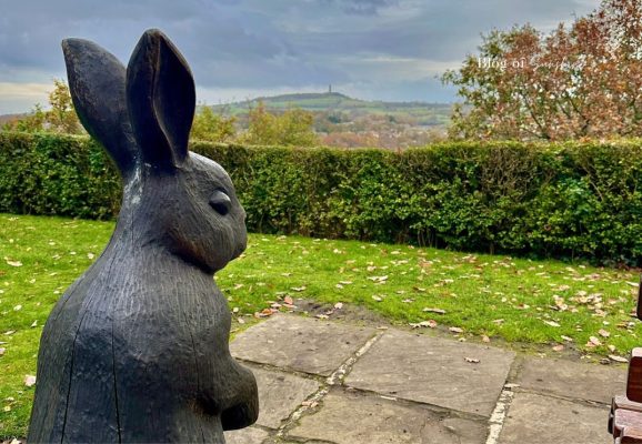 Large carved wooden rabbit sculpture at Beaumont Park Huddersfield, with autumn trees and distant countryside views.