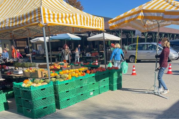 Colourful outdoor market in Poland with fruit and vegetable stalls, yellow striped canopies and shoppers.